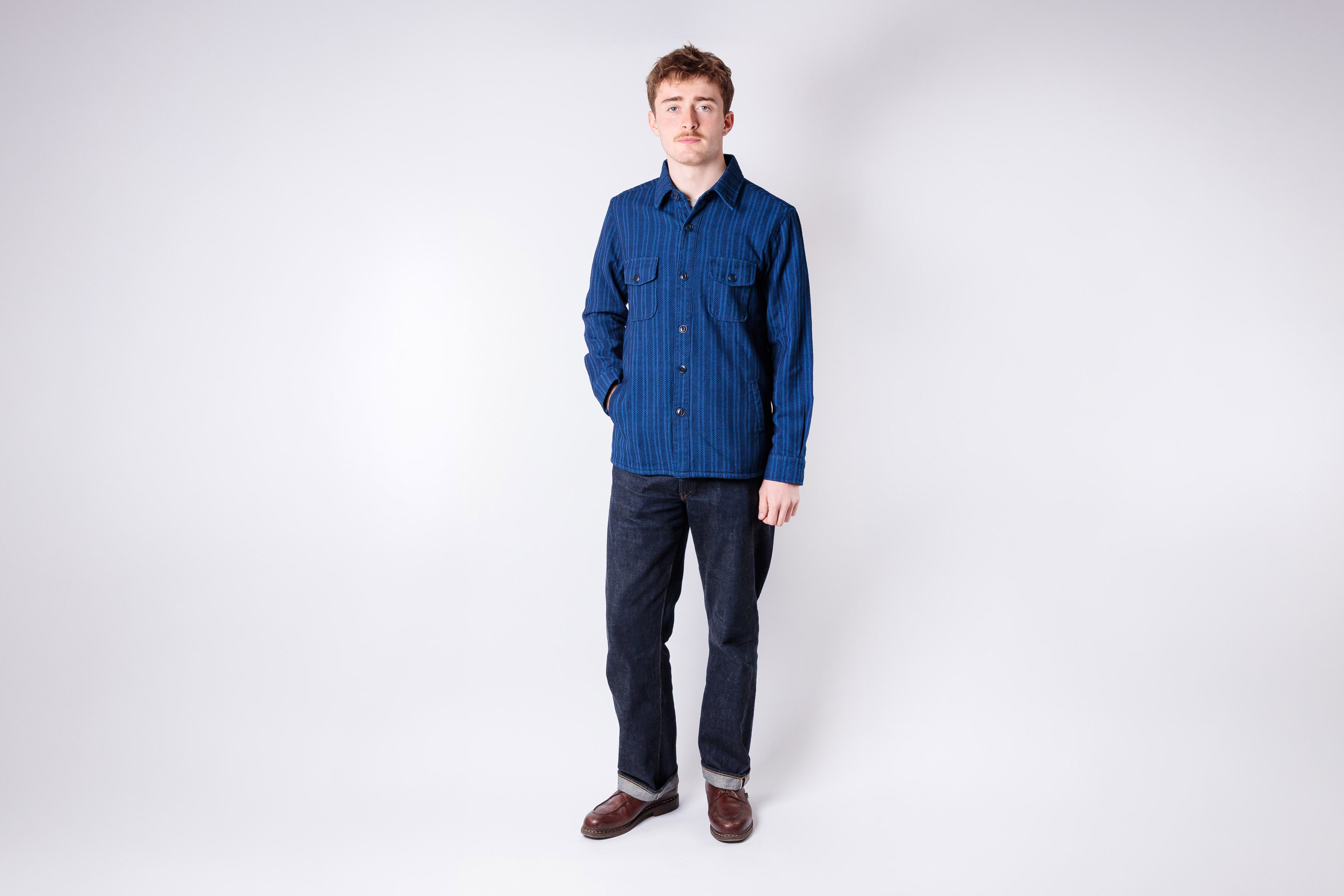 Man wearing a blue shirt and dark pants on a white background