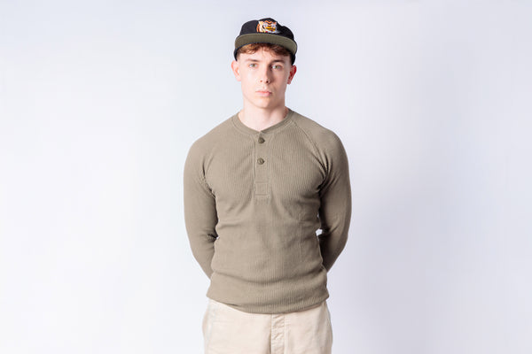 Man wearing a green long-sleeve shirt and beige cap against a light gray background