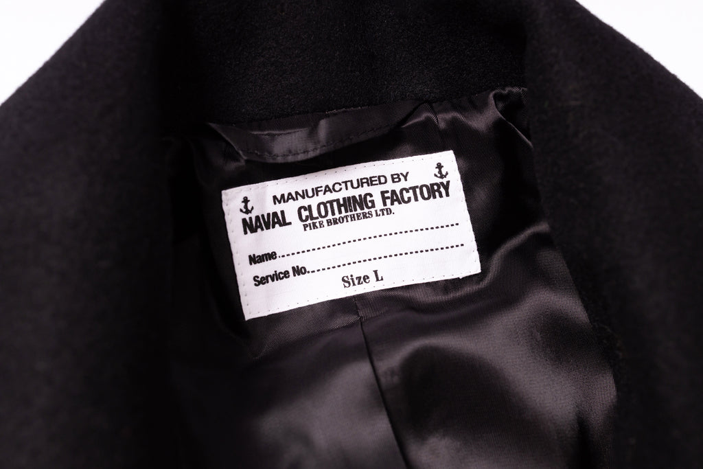 Label on a black garment indicating 'Manufactured by Naval Clothing Factory' with details.