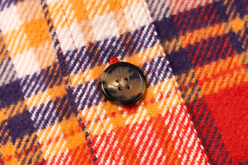 Close-up of a button on a plaid fabric with orange, purple, and red colors.