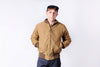 Person wearing a brown bomber jacket and cap on a white background