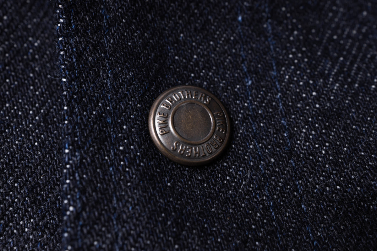 Close-up of a dark navy textured fabric with a round metallic button embossed