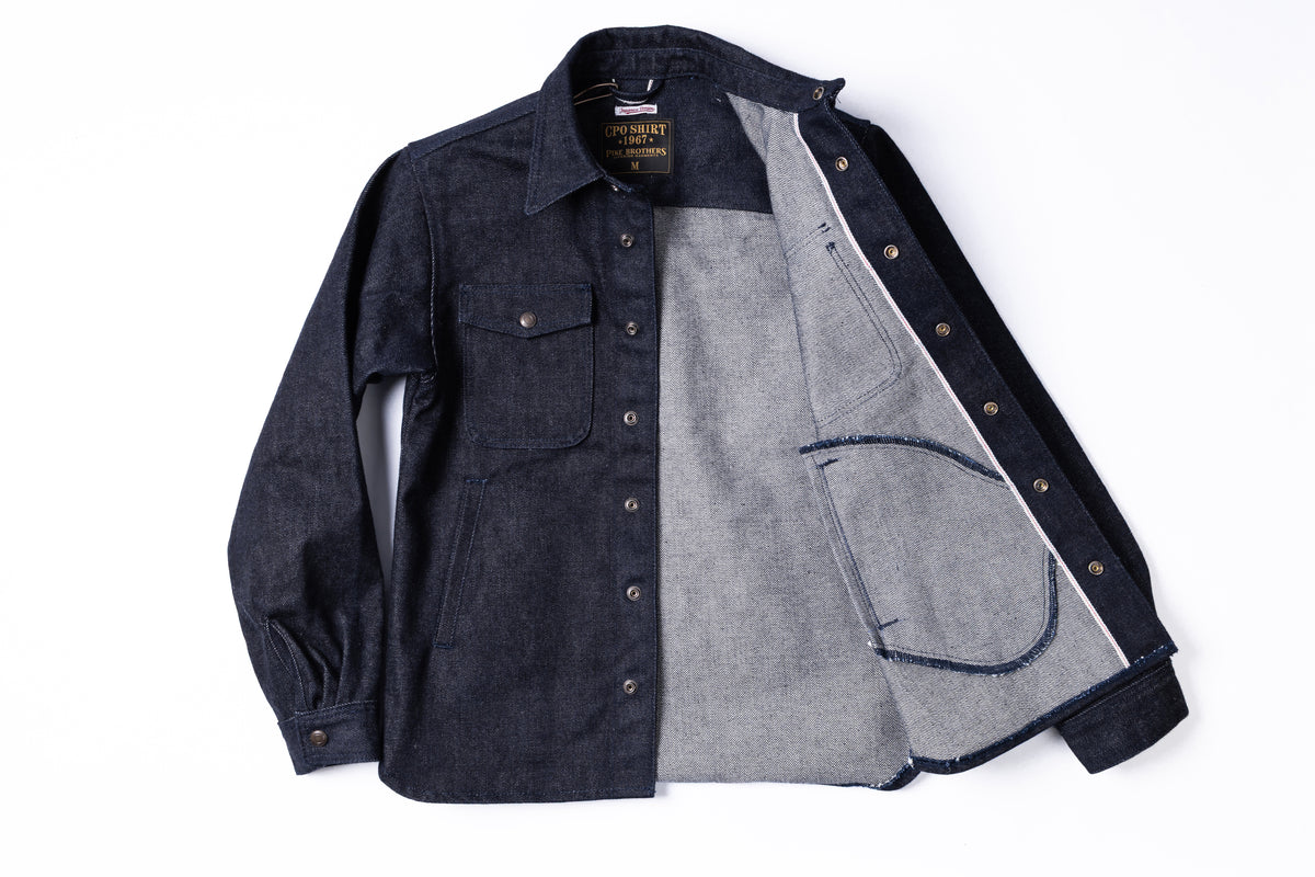 A dark indigo denim button-up shirt jacket from The Workwear Company, shown open to display its dual-layered construction with a lighter gray denim lining.