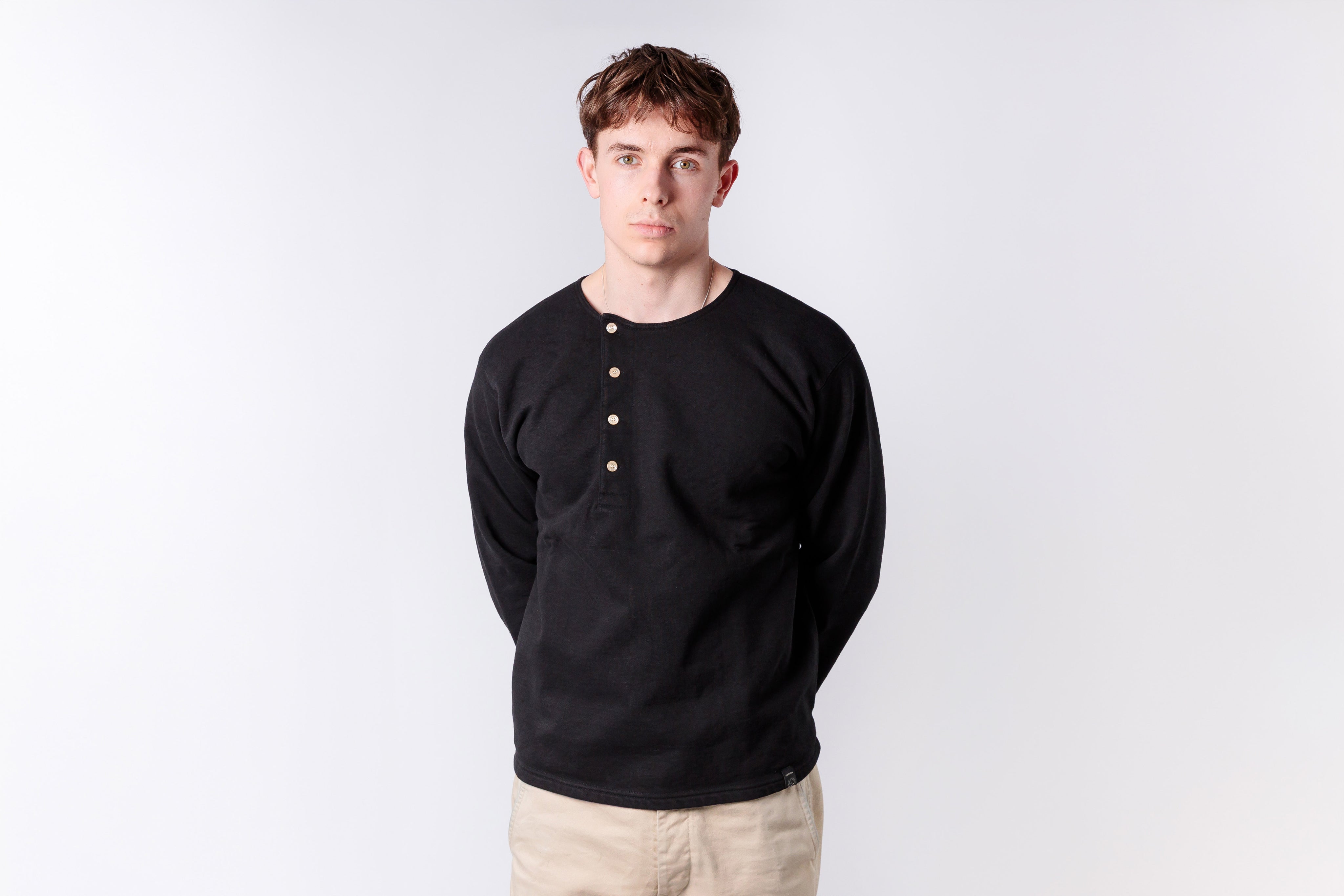 Man wearing a black long-sleeve shirt with beige buttons on a white background