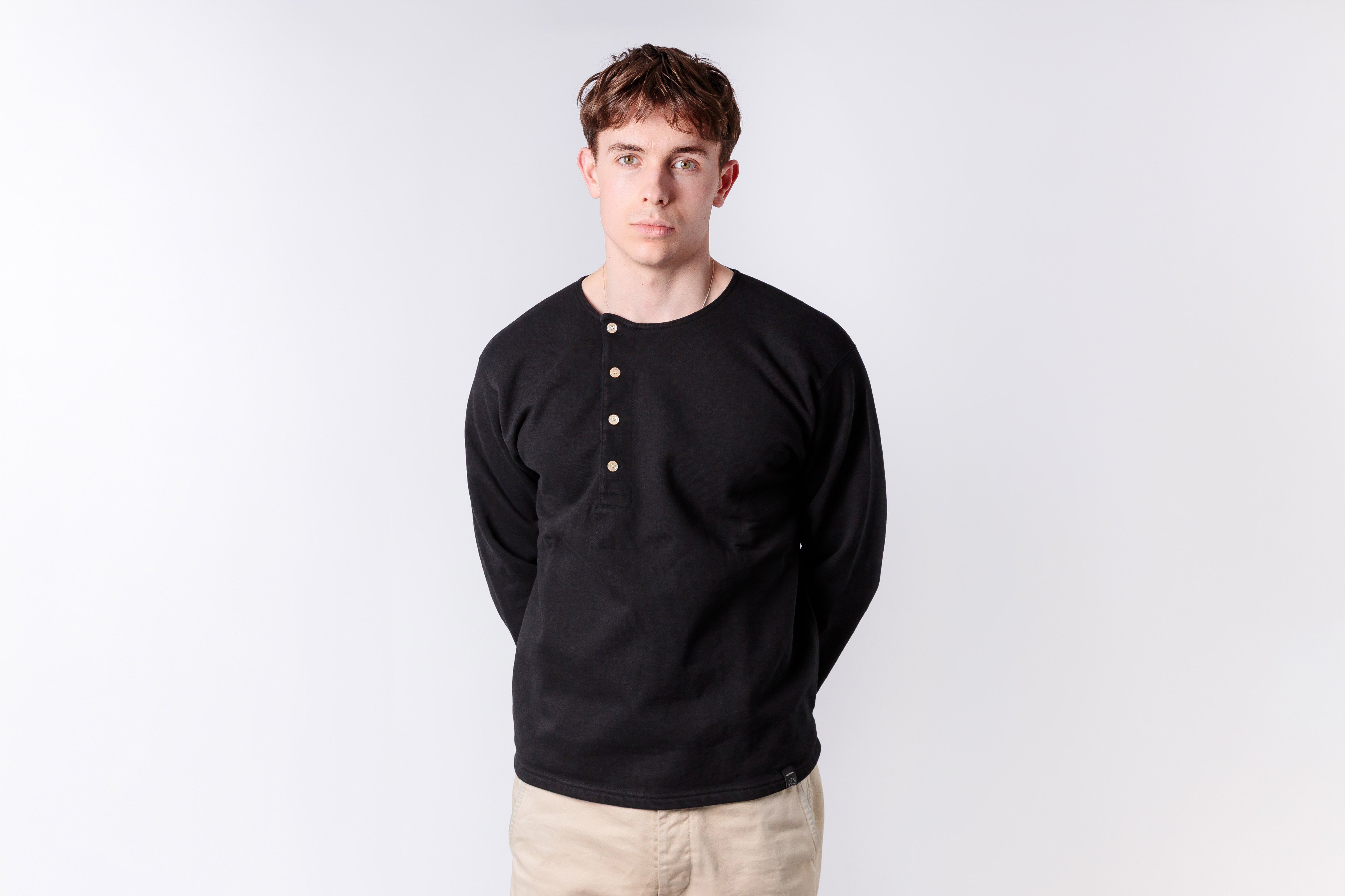 Man wearing a black long-sleeve shirt with beige buttons on a white background