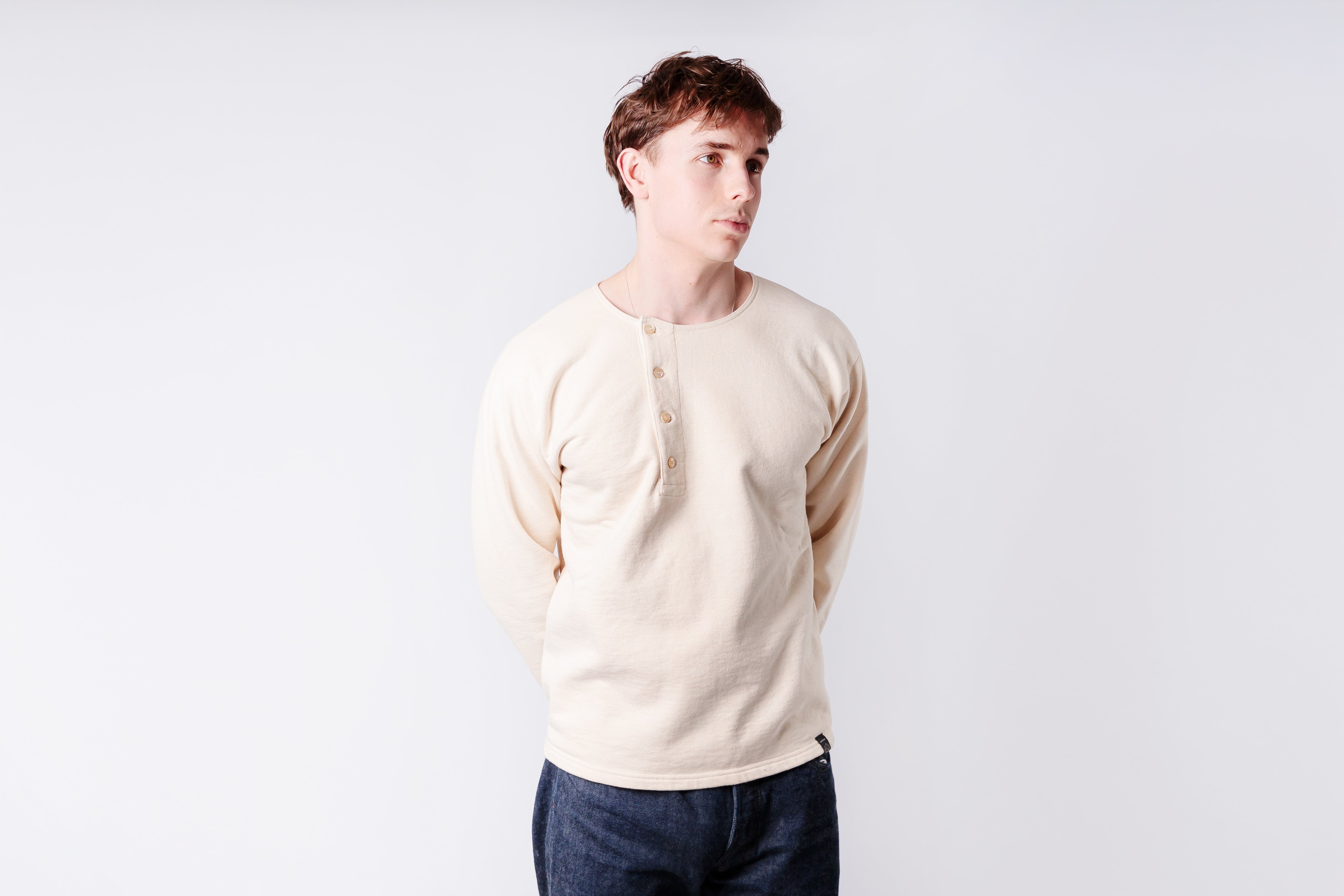 Man wearing a beige sweater and dark jeans against a white background
