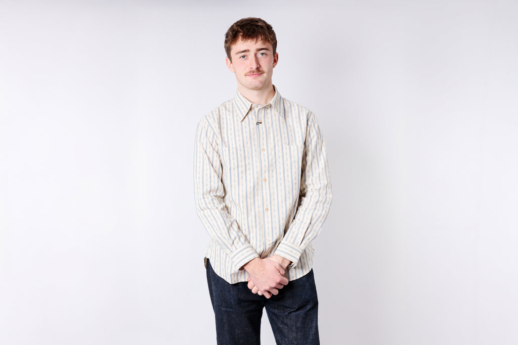Man wearing a striped shirt and dark pants against a plain background