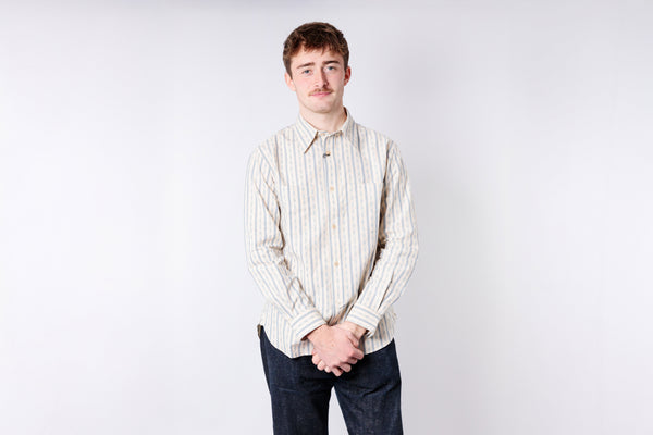 Man wearing a striped shirt and dark pants against a plain background