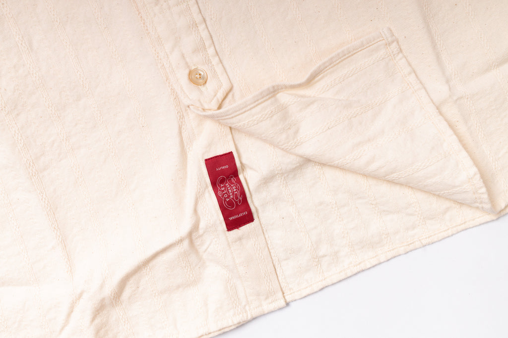 Close-up of a beige shirt with a red label on a white background