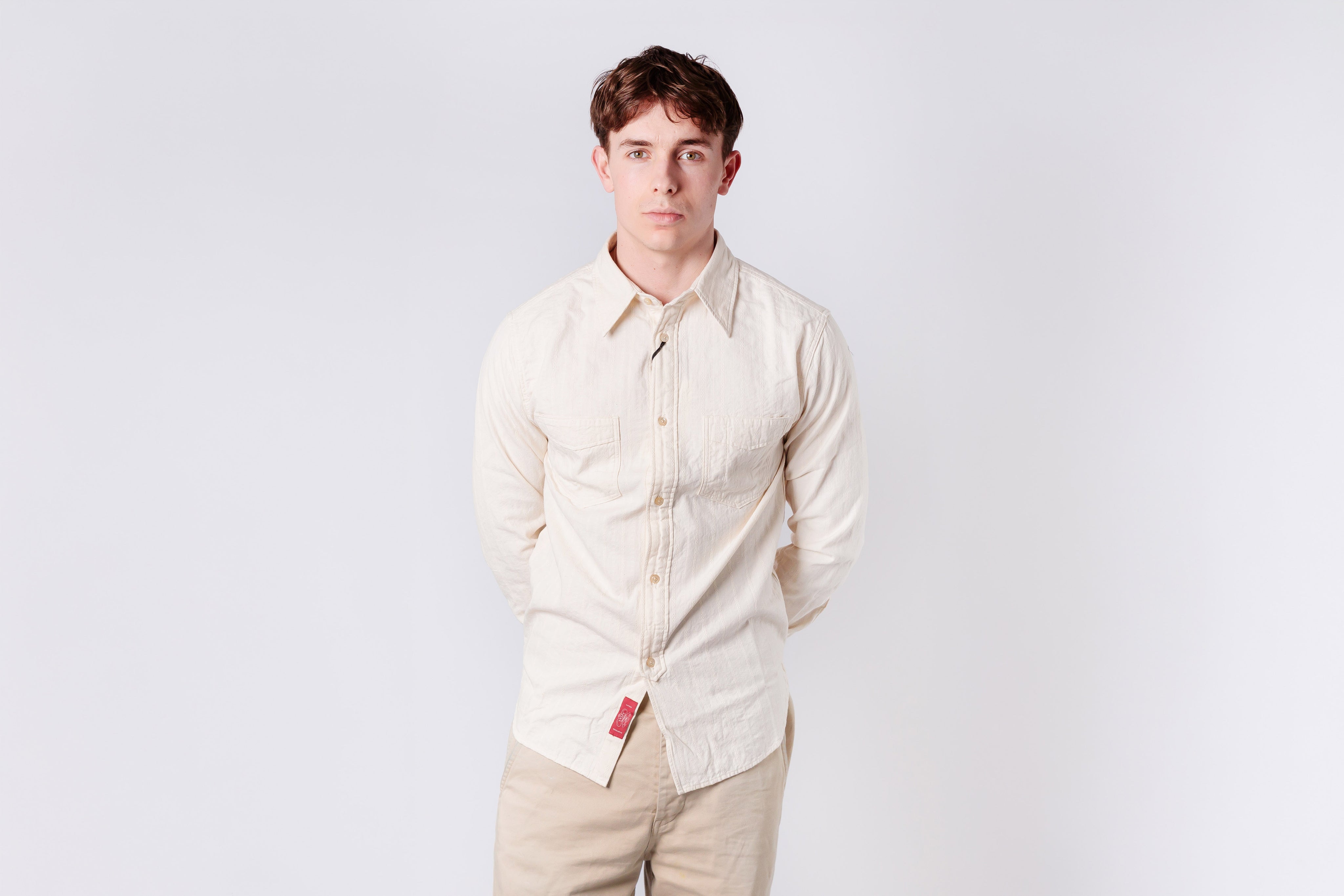 Man wearing a light-colored shirt and beige pants against a white background