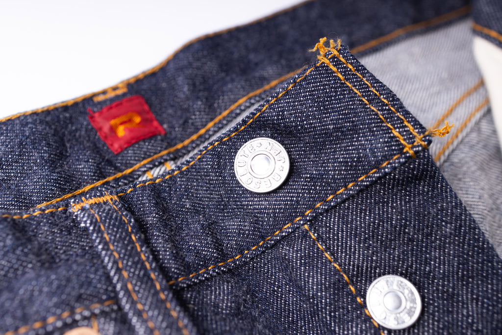 Close-up of a button on a pair of blue jeans with a red label.
