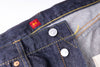 Close-up of a blue denim pocket with a red label and metal buttons on a white background