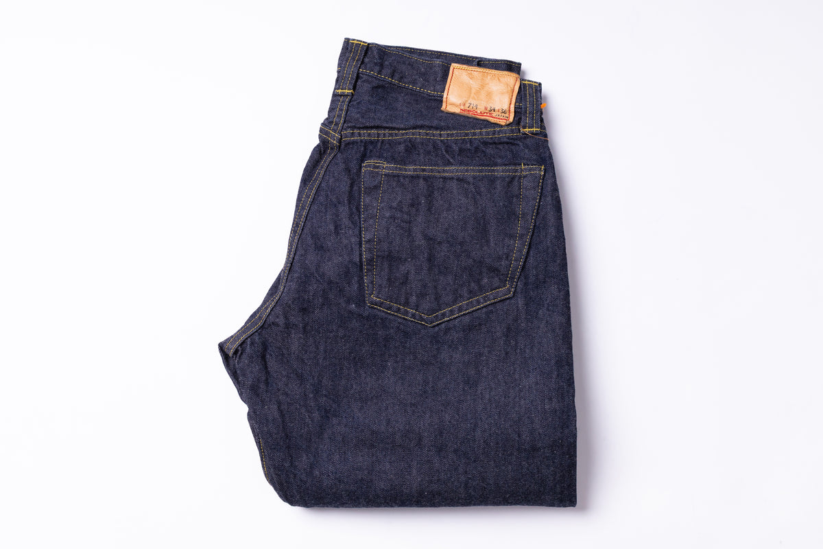 Dark indigo denim jeans folded to show the back pocket and waistband, with a tan leather brand patch, on a white background.