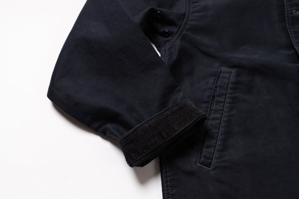 Close-up of a dark navy blue jacket or overshirt showing the sleeve cuff, buttoned collar, and a side pocket on a white background.