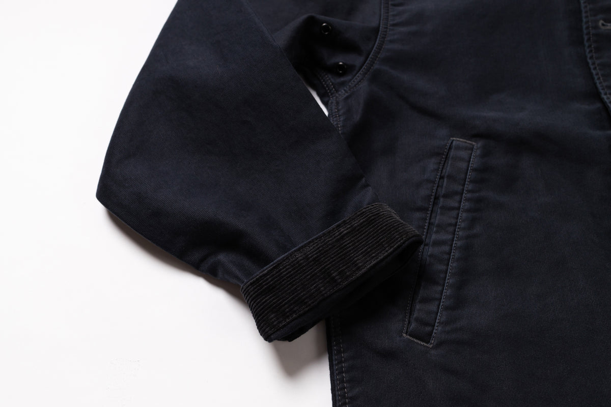 Close-up of a dark navy blue jacket or overshirt showing the sleeve cuff, buttoned collar, and a side pocket on a white background.