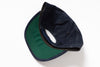 A folded dark navy blue denim cap with a green visor underside, photographed on a clean white background.