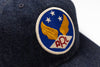 Close-up of a dark navy blue denim baseball cap featuring a circular embroidered patch with gold wings, white stars, and red 'RRL' lettering on a blue background.