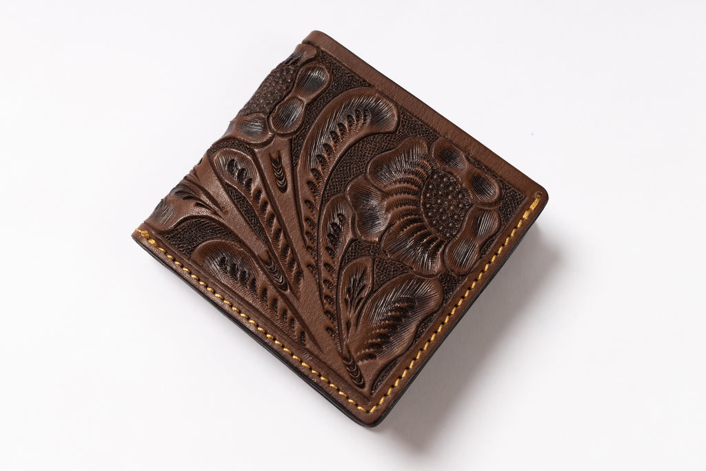 A brown tooled leather bifold wallet with floral and leaf embossed patterns and contrast stitching, shown on a plain white background.