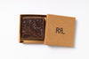 An embossed brown leather wallet with floral tooling, presented in an open kraft paper gift box with its lid showing the black monogram RRL