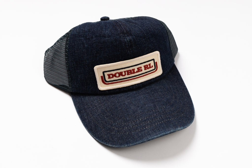 A dark indigo denim trucker hat with a beige rectangular patch on the front displaying 'DOUBLE RL' in red text, set against a plain white background.