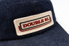 Close-up of a dark blue denim baseball cap featuring a rectangular embroidered patch on the front with the text 'DOUBLE RL' in red and black on a cream background.