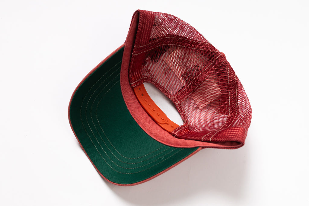 A red and green trucker cap with a red mesh back and a dark green visor, shown from an overhead angle on a white background.