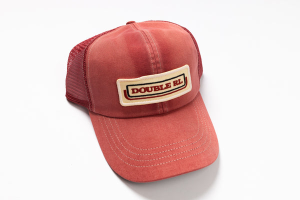 A washed red trucker hat with a beige patch on the front that reads 'DOUBLE RL' in red letters, set against a plain white background.