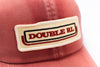 A close-up shot of a coral red baseball cap featuring a rectangular embroidered patch on the front with the text 'DOUBLE RL' in red, outlined with black and white borders.