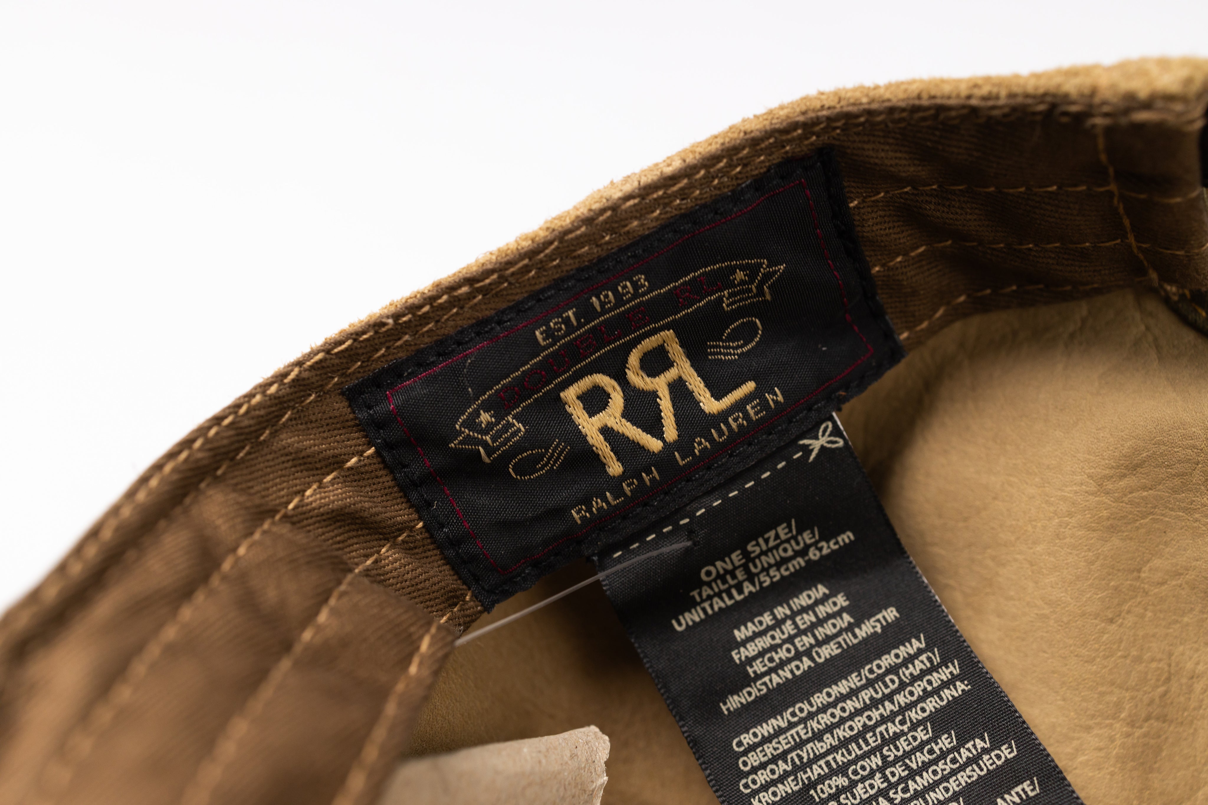 Close-up of a Ralph Lauren hat interior label, showing the black woven brand tag with gold lettering and a black information sewn label on tan fabric.