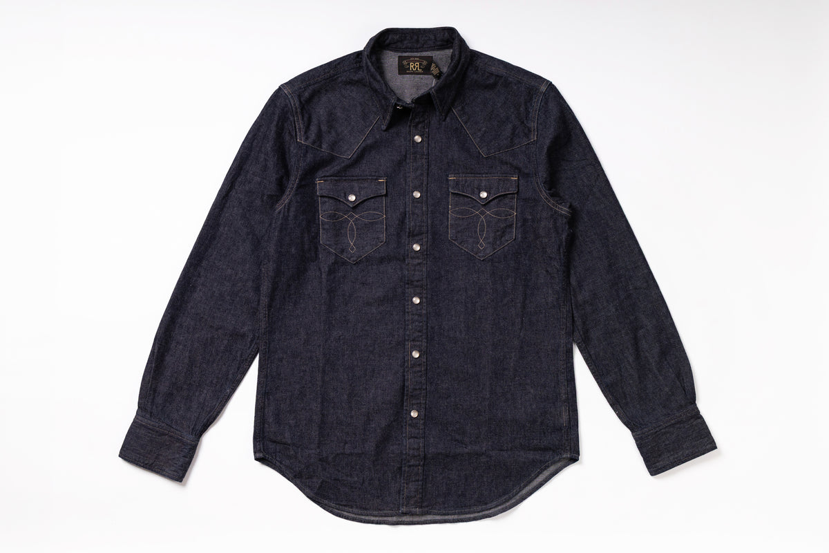 A dark indigo denim western-style shirt jacket with long sleeves, button-down front, and two chest pockets, laid flat on a white background.