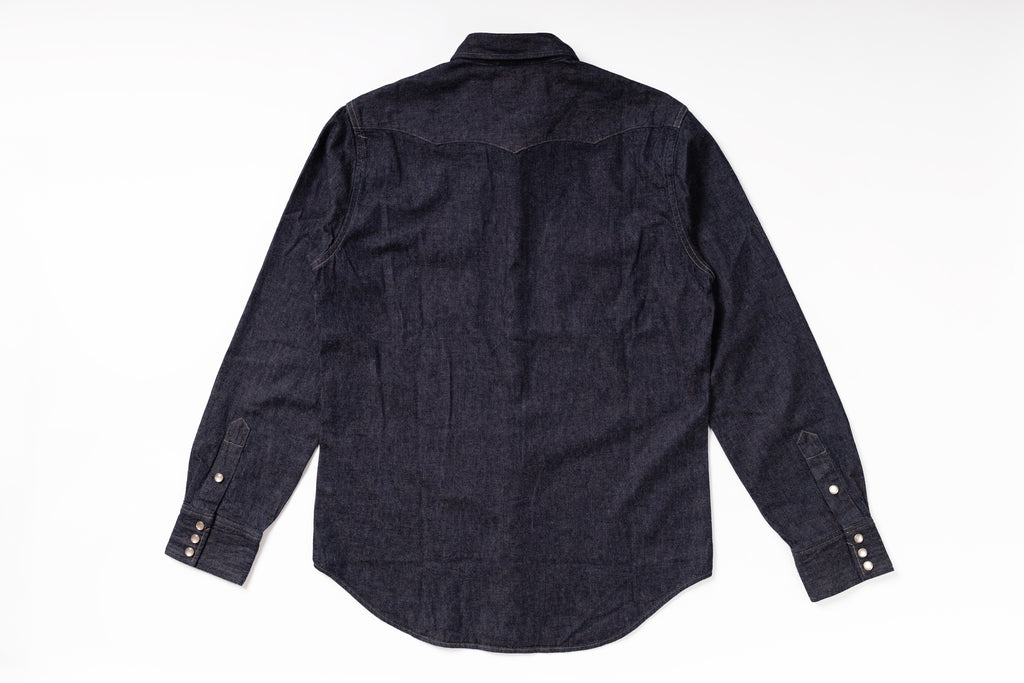 A dark indigo denim long-sleeve shirt shown from the back, laid flat on a white background.