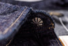 Close-up of dark indigo denim fabric with contrast tan stitching and a metallic fan-shaped rivet near the collar.