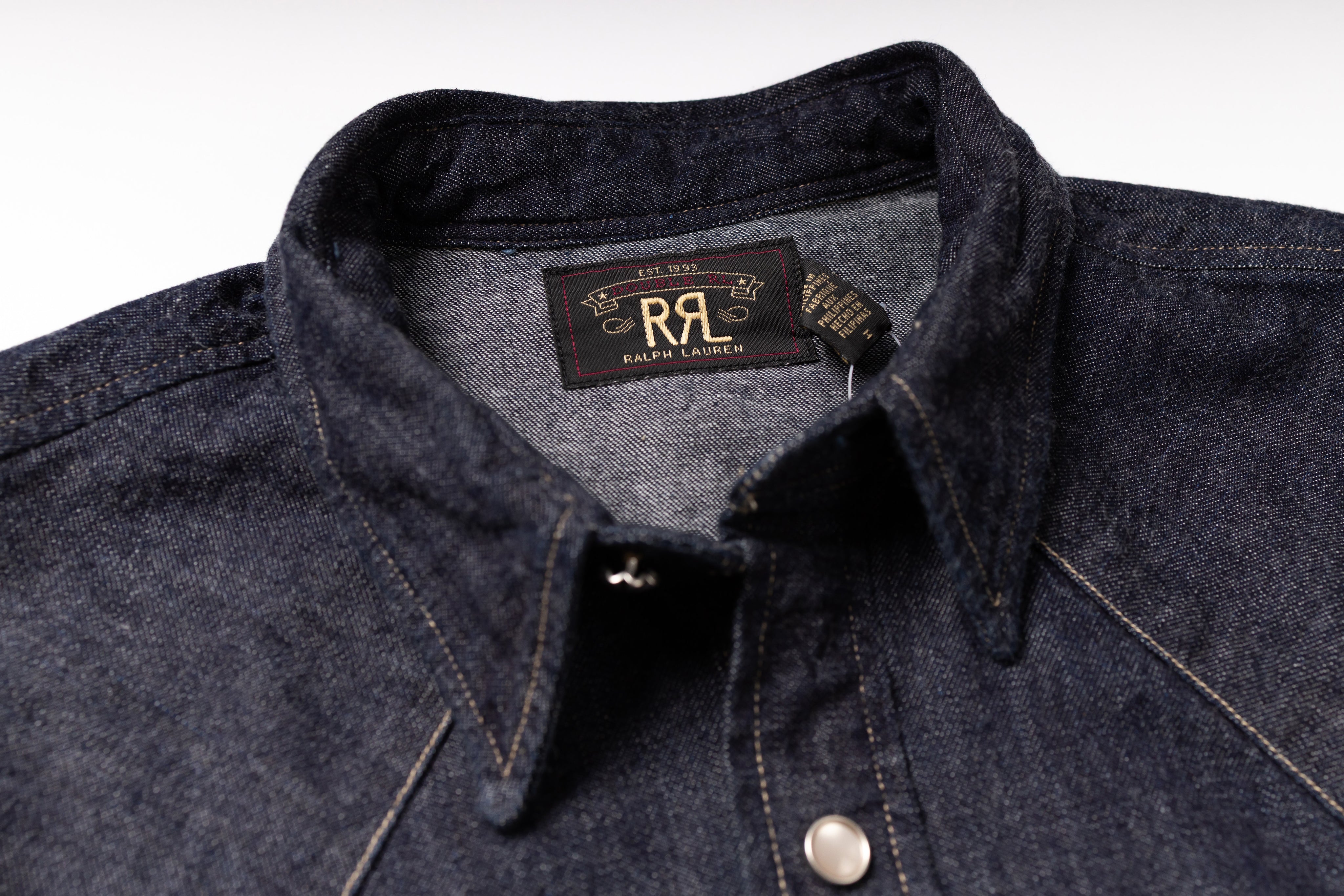 Close-up of a dark indigo denim button-down shirt collar with a visible neck label reading RRL Design.