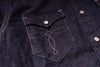 Close-up of a dark indigo denim jacket featuring a chest pocket with light tan contrast stitching and a silver snap button.
