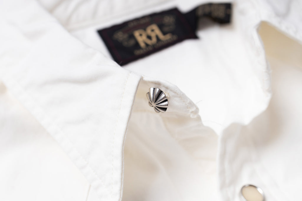 Close-up of a white button-up shirt collar with a metallic silver scalloped button and a black neck label reading RRL
