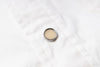 A small round silver-toned button with a beige center, placed on a white quilted fabric surface.