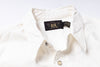 Close-up of a white button-up shirt collar with a black neck label featuring gold lettering.