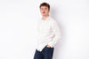 A man wearing a white long-sleeve button-up shirt and dark blue jeans, standing against a plain white studio background.