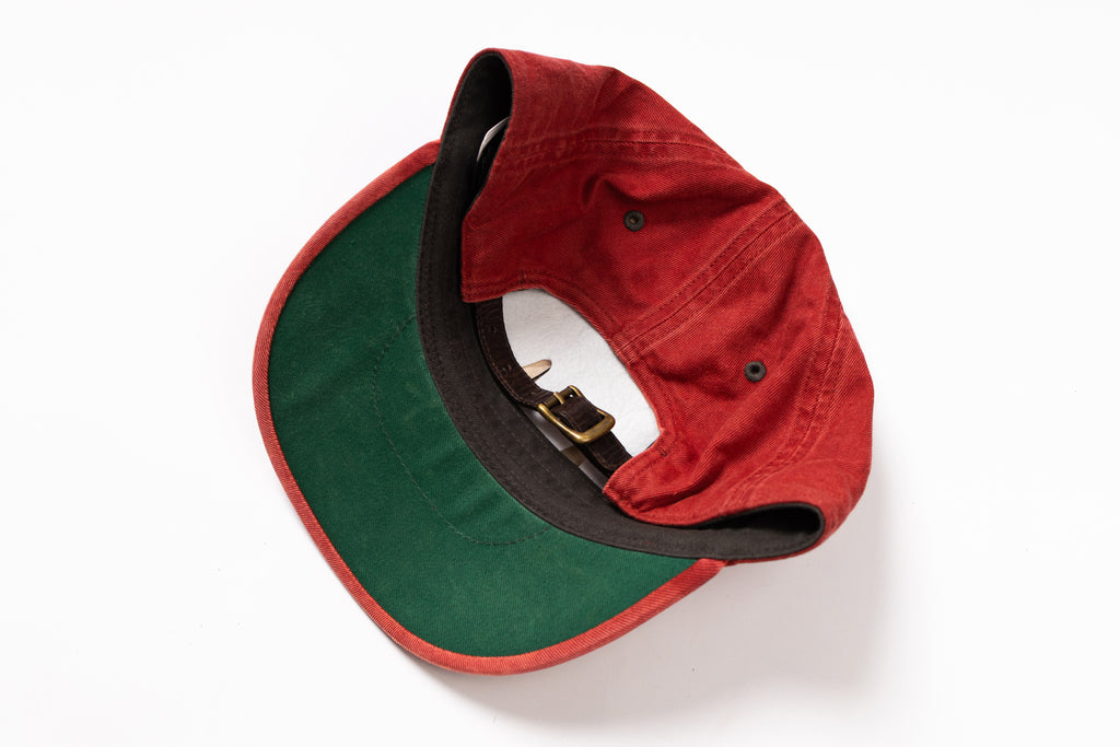 A red and green baseball cap shown from an overhead angle on a white background, displaying the red crown, green visor underside, black inner lining, and gold-tone buckle.