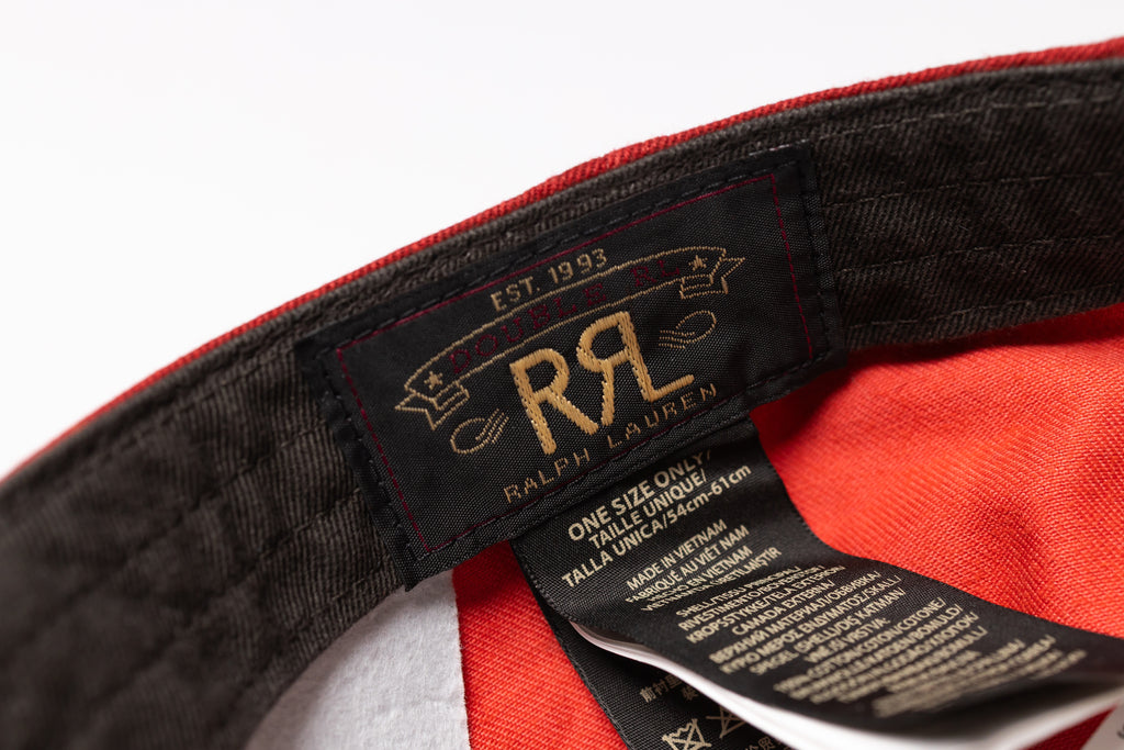 Close-up of the interior label of a Ralph Lauren one-size cap, showing the black woven brand patch with gold embroidery and the attached black care tag against a red and white fabric interior.