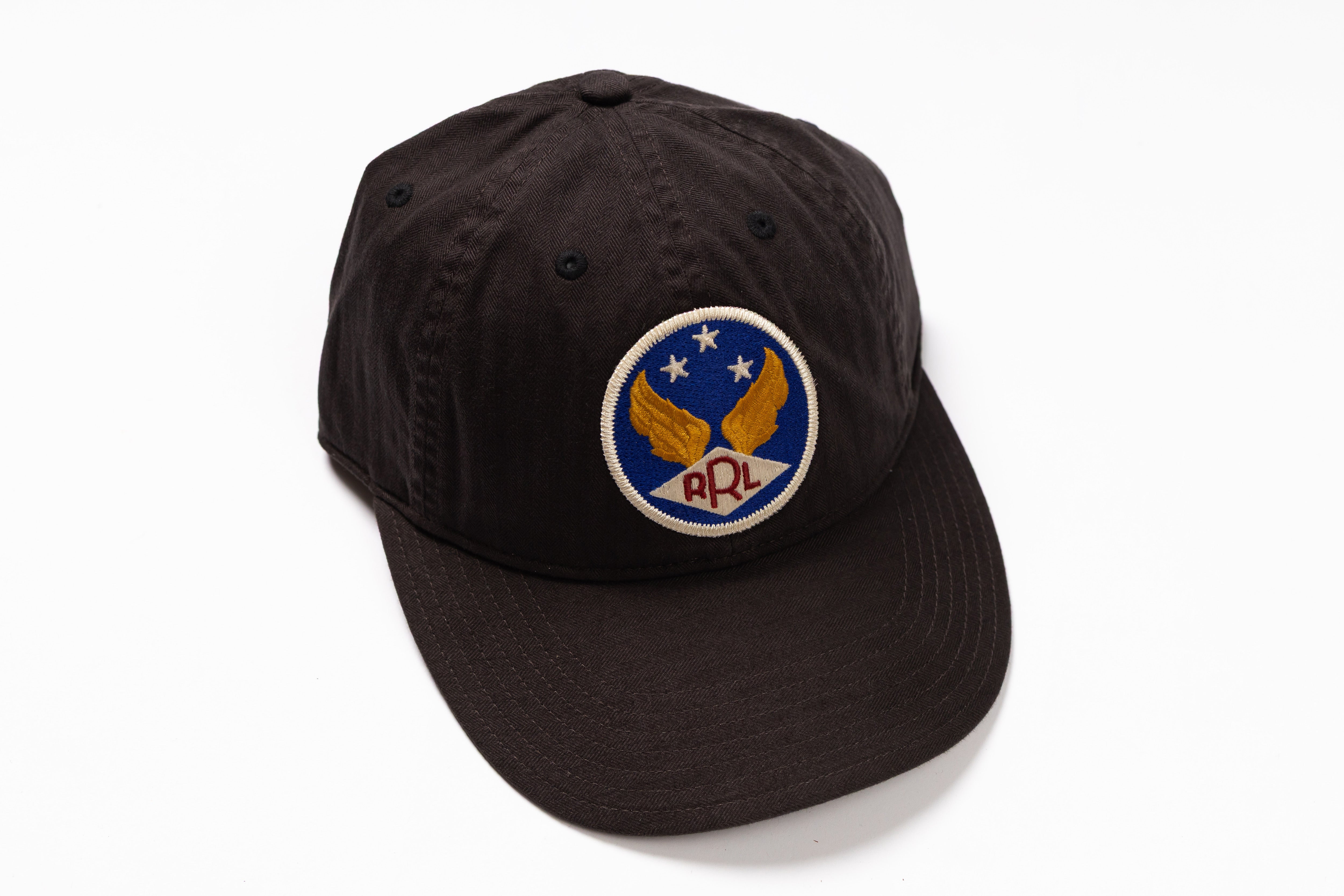 A black cotton baseball cap featuring a circular embroidered patch on the front with a blue background, gold wings, white stars, and the letters 'RPL' in red.