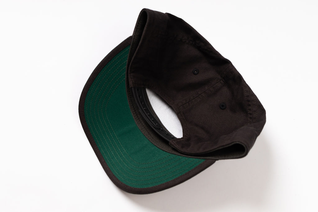 A folded baseball cap shown from the underside, featuring a dark green visor with black piping and a black crown, photographed on a clean white background.