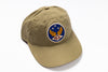 A khaki baseball cap featuring a circular embroidered patch on the front with wings, stars, and the letters 'RRL' on a white background.