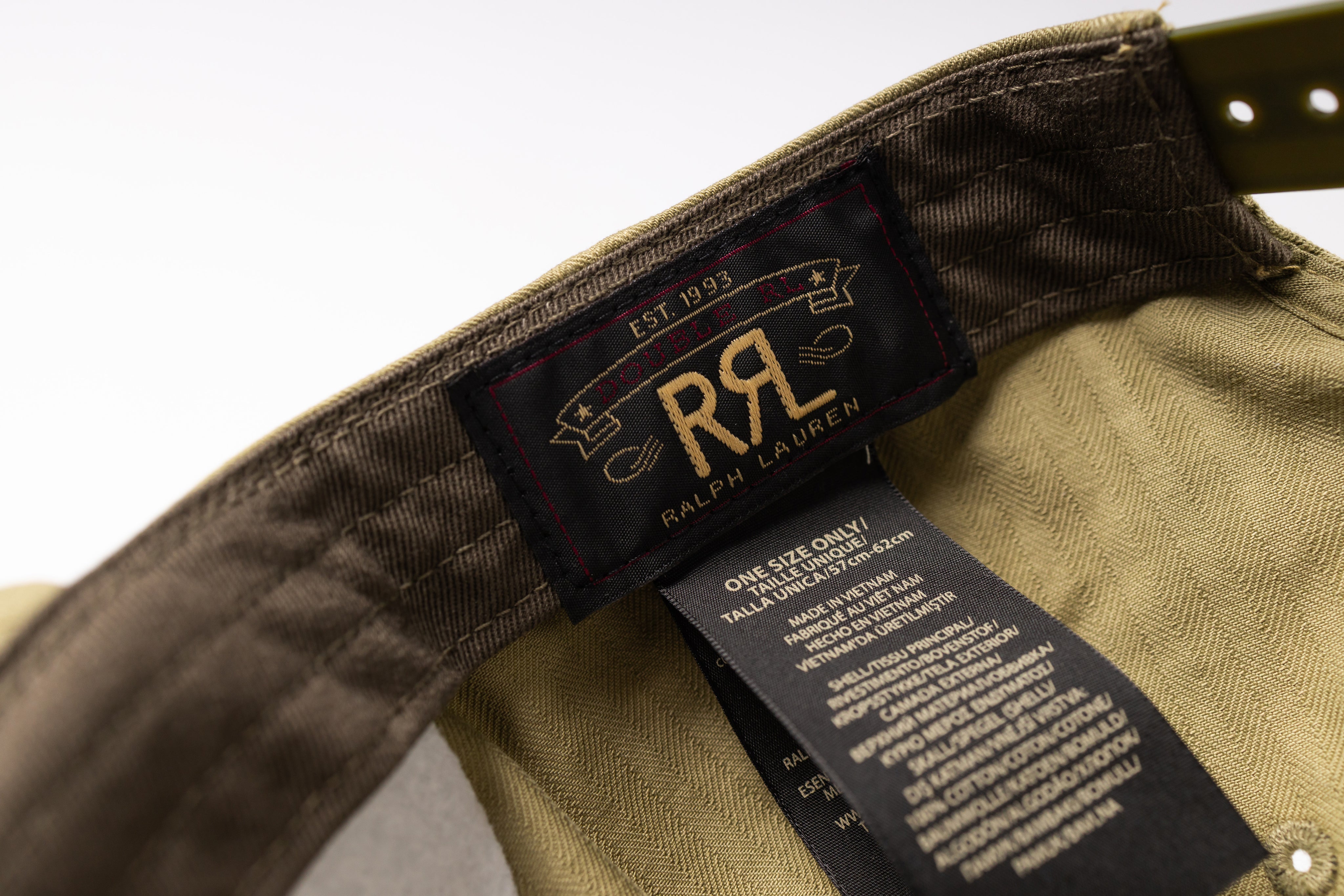 Close-up of the inside collar of a Ralph Lauren garment, showing the black neck label with gold 'RL' logo and a hanging care tag on olive green fabric.