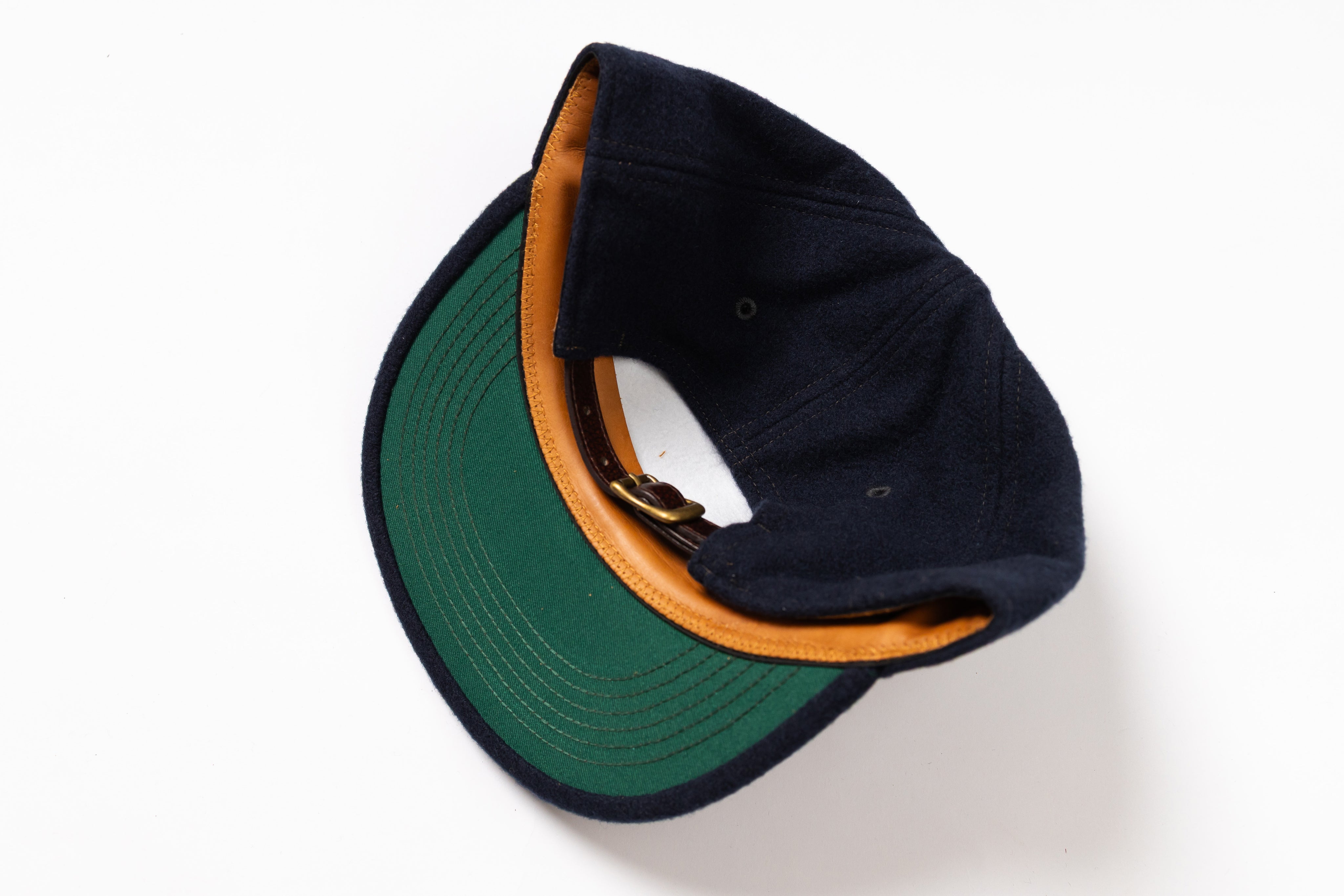 A dark navy blue baseball cap with a green visor and a tan leather-like trim along the edge, shown from an overhead angle on a white background.