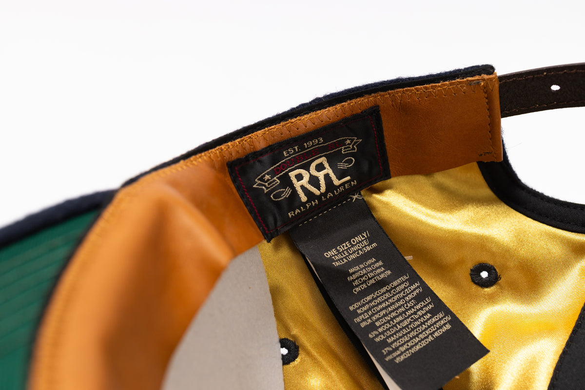 Close-up of the interior of a baseball cap showing a black brand patch with 'Ralph Lauren' and 'EST. 1993', a gold satin lining, and a black size tag.