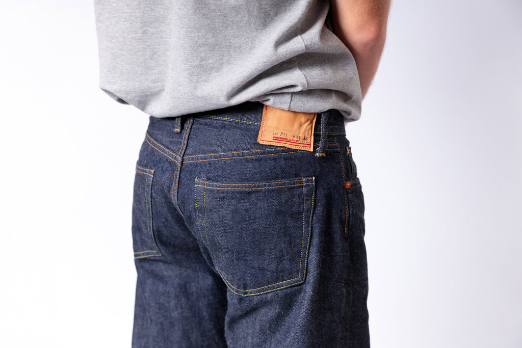 Person wearing blue jeans with a visible brand label on a white background