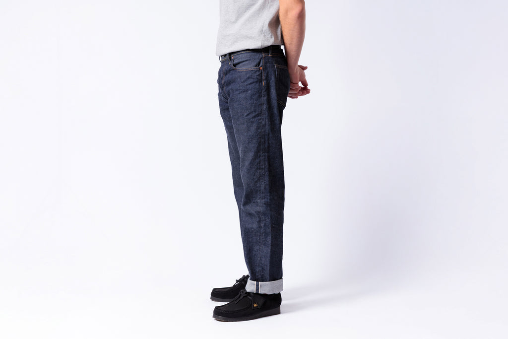Person wearing dark blue jeans and black shoes on a white background