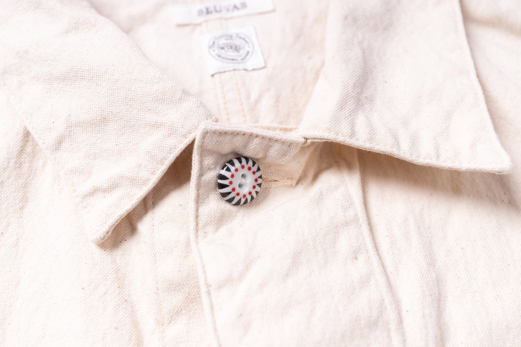 Close-up of a light-colored shirt with a button and brand label.