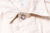 Close-up of a light-colored shirt with a button and brand label.